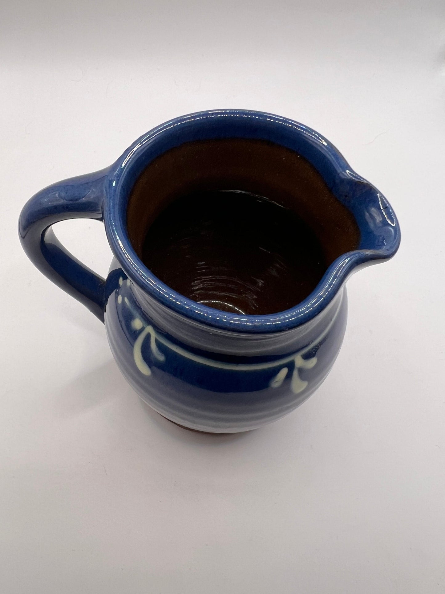 Studio pottery terracotta blue glazed milk water jug. White leaf detail.